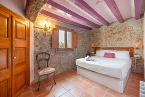 A bedroom with a stone wall, wooden door, and a bed with white bedding. - Apartment 'Cal Capdevila Blau' with Mountain View, Wi-Fi and Air Conditioning (Pira)