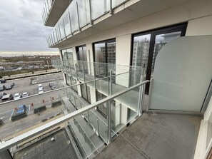 Ein modernes Gebäude mit einem Glasbalkon mit Blick auf einen Parkplatz und entfernte Bauten.