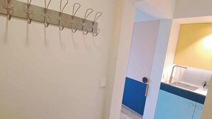 A hallway with a coat rack, a door leading to a kitchen with blue cabinets, and a tiled floor. - Coastal Couple Hideaway in Oostduinkerke (Koksijde)