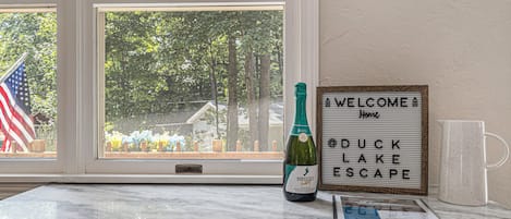 Une bouteille de vin Barefoot, un panneau d’accueil et une tasse posée sur une table en marbre près d’une fenêtre.