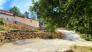 Un muro de piedra que conduce a un edificio con techo de tejas rojas, camino de grava y valla de madera.