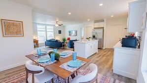 A modern kitchen with white cabinets, a central island, and a dining area with a wooden table and white chairs.