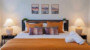 A neatly made bed with a brown blanket, two pillows, and a rolled towel. There are two bedside tables with lamps, and three framed pictures on the wall above the bed.