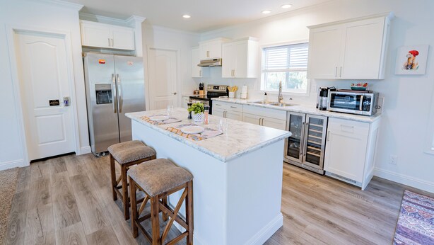 A modern kitchen with white cabinetry, a central island with stools, a stainless steel refrigerator, and a microwave.