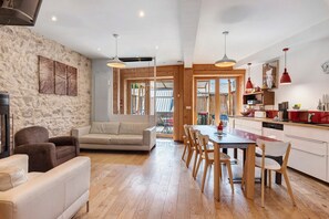 A modern interior with a stone wall, a sofa, a dining table with chairs, and a kitchen area. - L’Authentique du Vercors, Wood Charm & Modern Comfort (Villard-de-Lans)