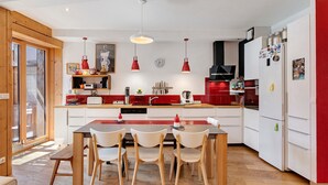 Una cocina moderna con una isla central, luces colgantes rojas y un área de comedor con cuatro sillas.