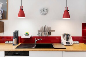 Eine moderne Küche mit schwarzem Arbeitsplatz, einem Geschirrspüler von Siemens, einer Kaffeemaschine, einem Wasserkocher und einem weiteren Wasserkocher auf dem Herd.