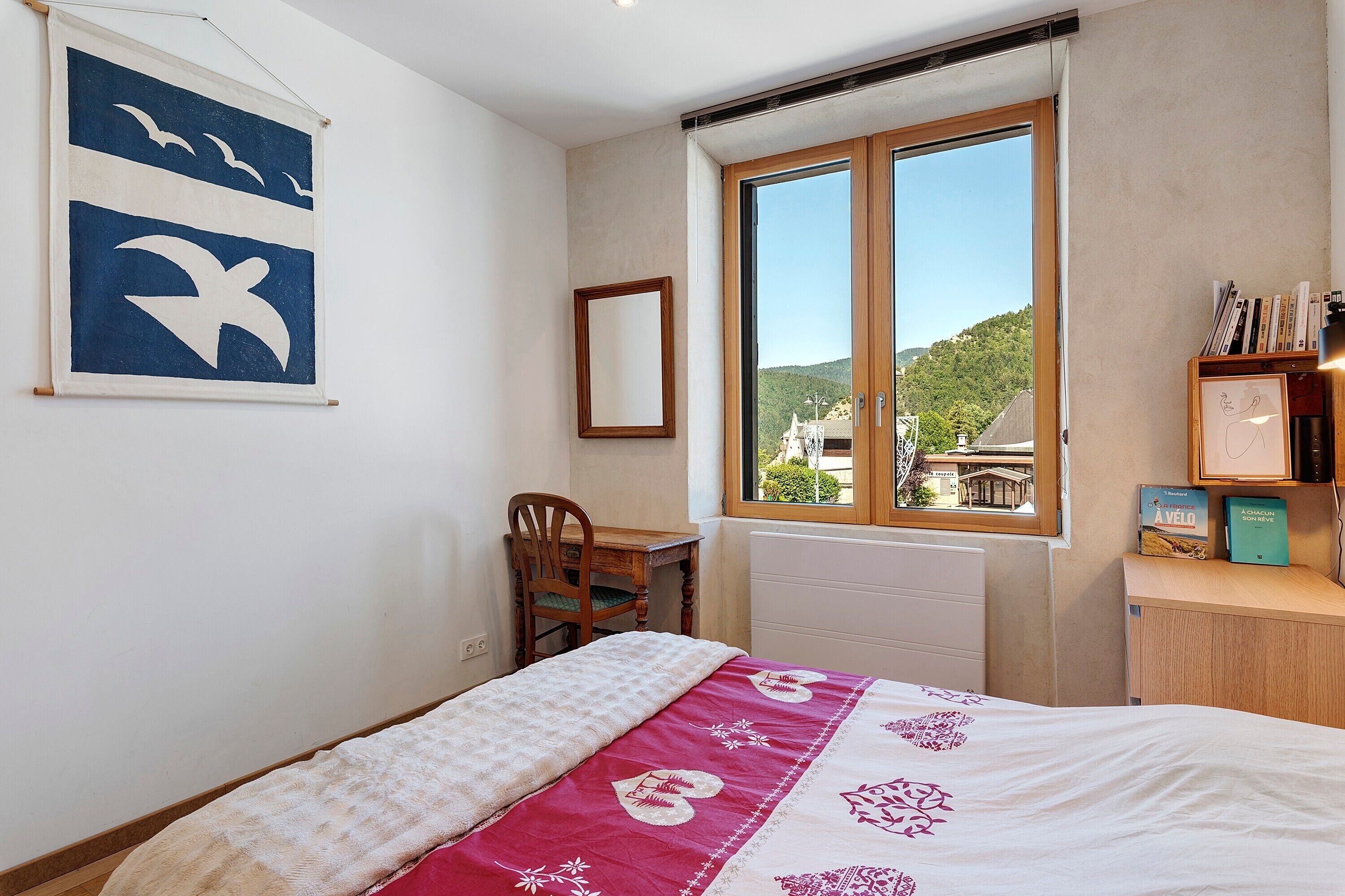 Ein Schlafzimmer mit Bett, Schreibtisch, Stuhl, Fenster mit Aussicht und Bücherregal.