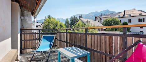 A balcony with a metal grill, a blue chair, a small table, and a pink hammock.