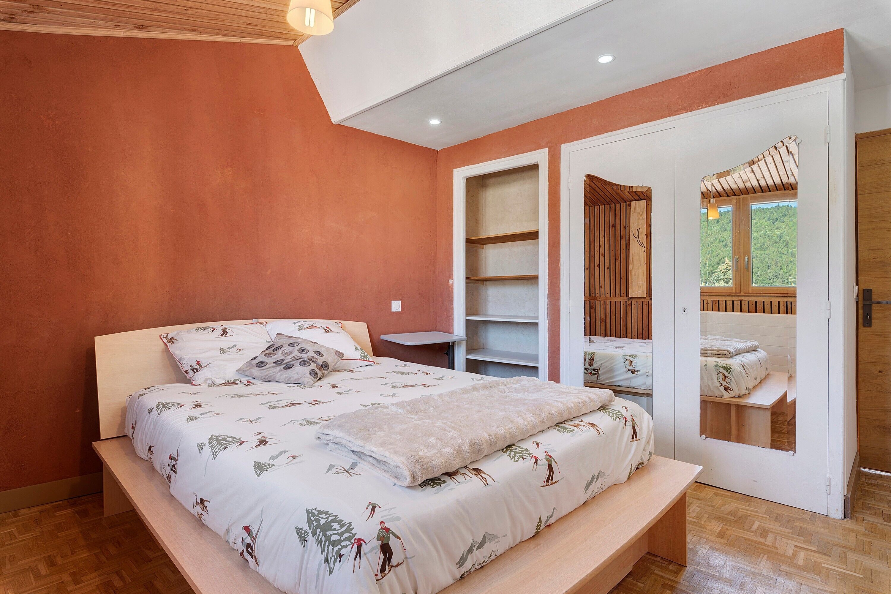A bedroom with a bed, a bedside table, a wardrobe, and a door leading to an outdoor area.