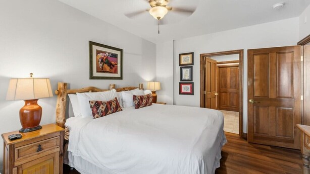 Une chambre à coucher avec un lit, une tête de lit en bois, des lampes de chevet, un ventilateur de plafond et une porte.