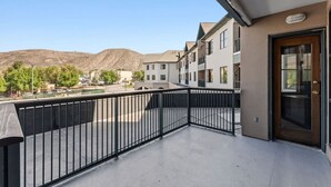 Un balcon doté d’une balustrade en métal, une porte avec un panneau de verre et une vue sur un quartier résidentiel, avec des immeubles et une montagne en arrière-plan.