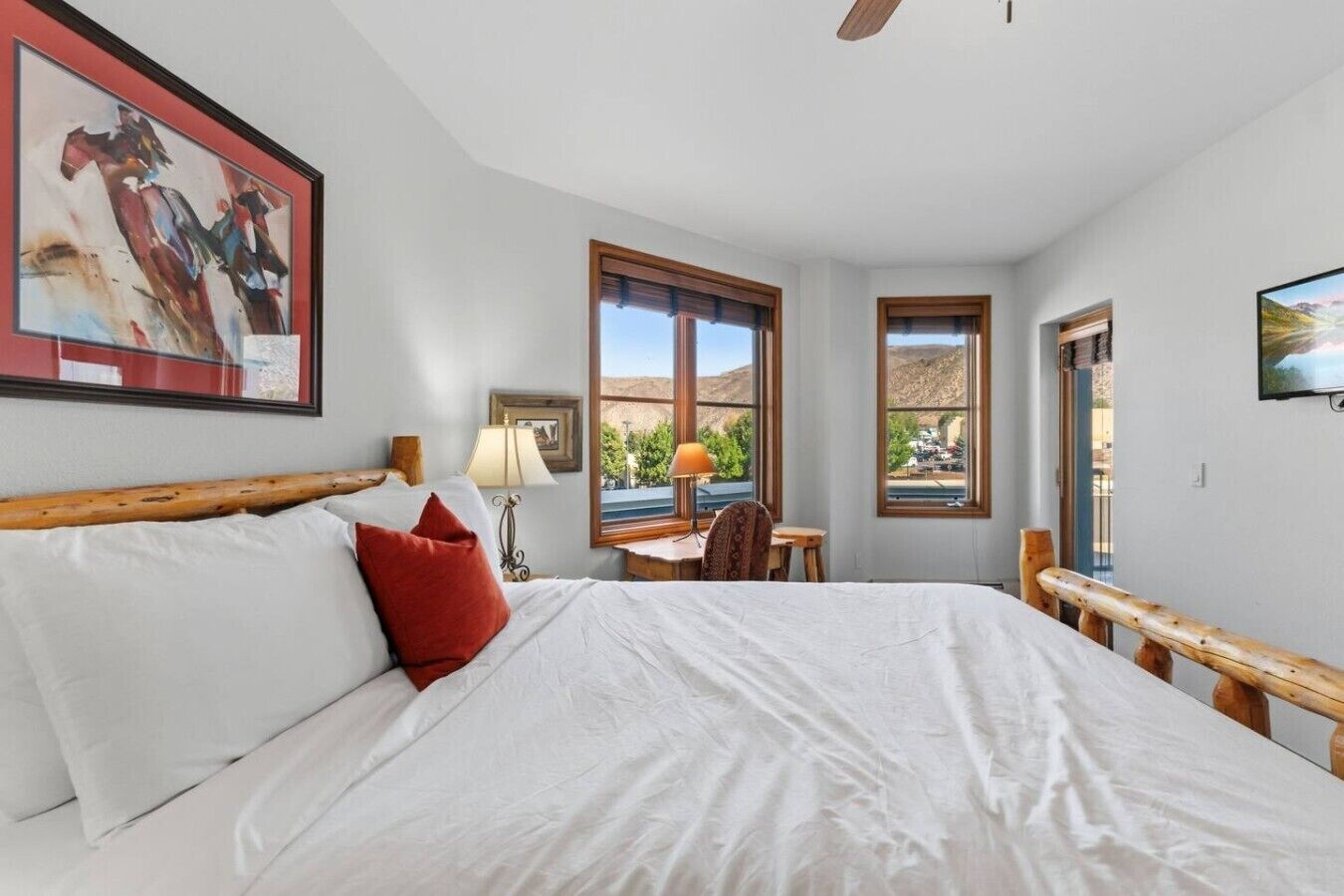 Un dormitorio con una cama grande, un escritorio y una silla. Hay ventanas con vistas al exterior.