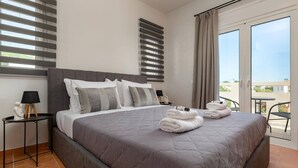 Habitación de hotel con una cama grande, una mesita con lámpara, una mesita de noche y vistas al exterior.