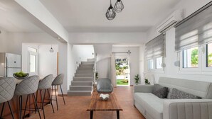 Una sala de estar moderna con un sofá, una zona de comedor con sillas, una escalera y un equipo de aire acondicionado.