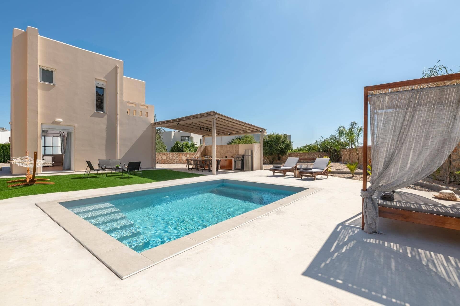 Area piscina moderna con pergola, poltrone relax e zona salotto coperta.