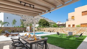 Un espacio al aire libre techado con piscina, mesa y sillas.