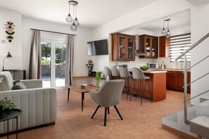 A modern kitchen with wooden cabinets, a dining area with a table and chairs, and a staircase leading to an upper level. - Villa Avia Pefkos by Villa Plus (Pefki)