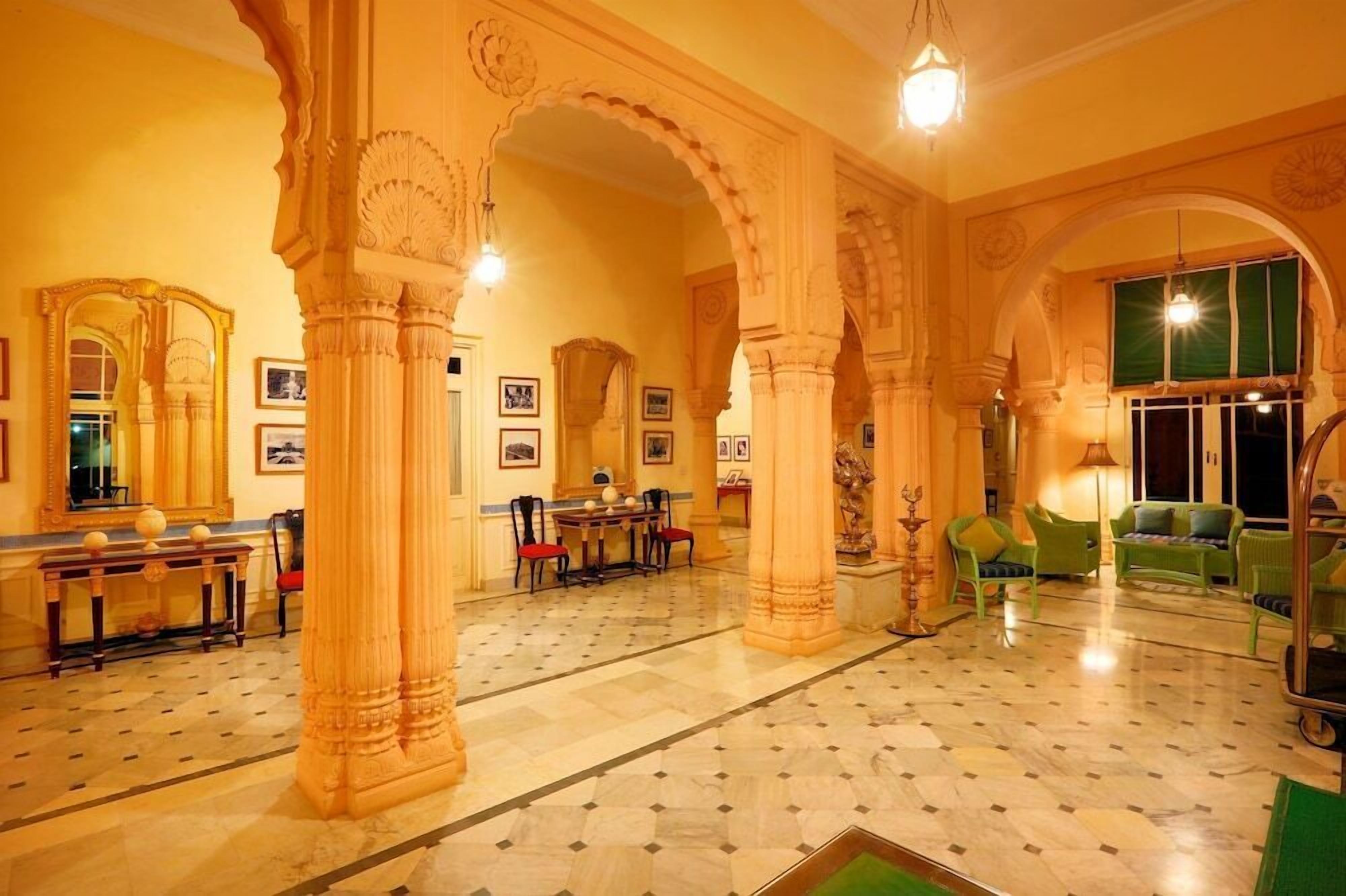 A lobby with ornate columns, a marble floor, and green upholstered furniture.
