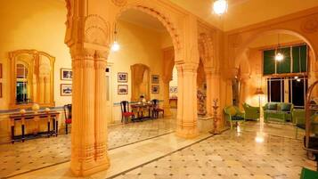 A lobby with ornate columns, a marble floor, and green upholstered furniture.