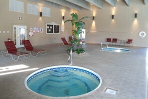 Ein Poolbereich im Innenbereich mit zwei Schwimmbecken, roten Liegestühlen und einer großen Pflanzengruppe.