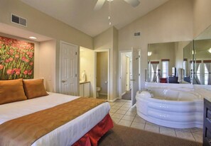 Ein Hotelzimmer mit Bett, Badezimmer mit Whirlpool, großem Spiegel und einer Tür zu einem weiteren Raum.