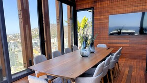 A modern dining area with a wooden table and chairs, large windows, and a view of the city. - Departamento con chalet (Puerto Vallarta)