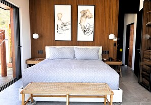 Ein Schlafzimmer mit einem großen Bett, zwei an der Wand befestigten Kunstwerken, Nachttischen mit Lampen und einer Holzbank.