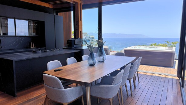 A modern kitchen with a large island, a dining area with a wooden table and chairs, and a view of the sea. - Departamento con chalet (Puerto Vallarta)