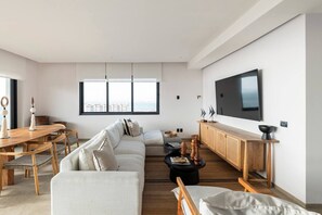 Ein modernes Wohnzimmer mit großem Fernseher, einer Couch, einem Esstisch und Blick auf die Stadt.
