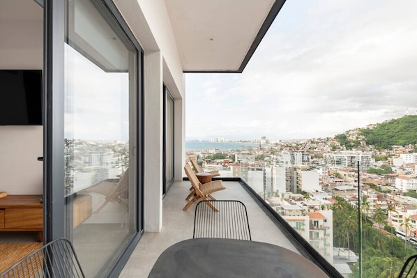 Ein moderner Balkon mit Stadtblick, großen Fenstern und einer Essecke mit Stühlen und Tisch.