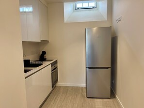 Una cocina compacta con armarios blancos, horno integrado y refrigerador de acero inoxidable.