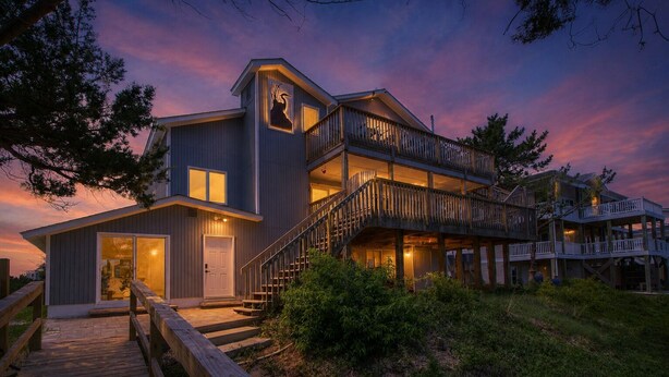 Une maison à deux étages avec une terrasse en bois, un escalier et une grande porte d’entrée.