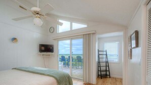 Une chambre à coucher avec un lit, un ventilateur de plafond, une télévision et une vue sur l’extérieur.