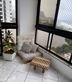 Ein Balkon mit Sitzgelegenheit mit Kissen, einer Topfpflanze und einem Holzschemel.