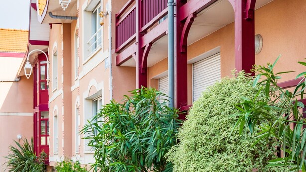 Un edifici amb una porta vermella, finestres blanques i balcons amb baranes vermelles.