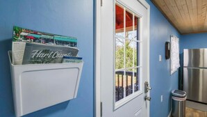A kitchen with a stainless steel refrigerator, a trash can, and a window with a view of greenery.