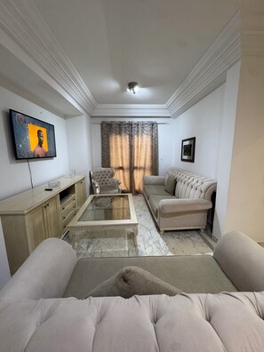 Ein Wohnzimmer mit Sofa, Sessel, Couchtisch, Fernseher und Vorhängen.