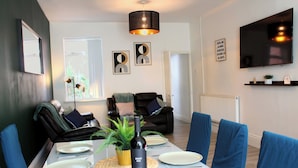 A dining area with a table set for four, a bottle of wine, and a potted plant. - 3-Bed Bearwood | Midland Met, No CAZ, Free Parking (Smethwick)