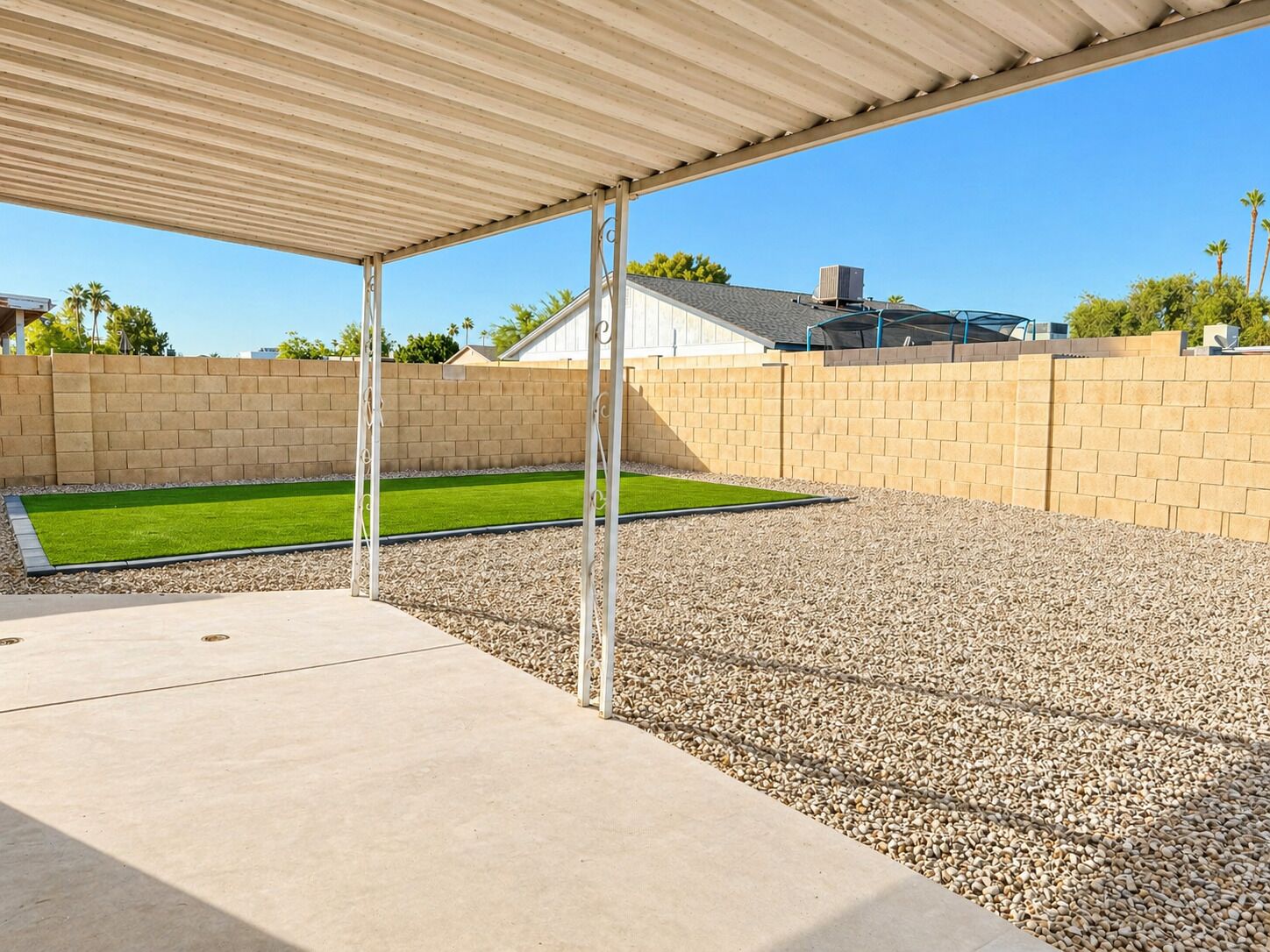 Ein überdachter Patio-Bereich mit Betonboden, Kiesfläche und einer kleinen Rasenfläche aus künstlichem Gras.