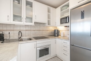 A modern kitchen with white cabinetry, a stainless steel refrigerator, a built-in oven, a microwave, and a coffee maker.