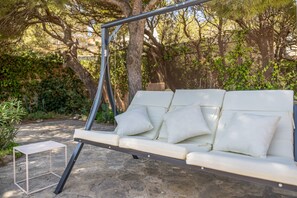 A white outdoor sofa with cushions, a metal swing frame, and a small white table.