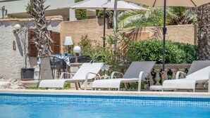 A poolside area with lounge chairs, a table, and umbrellas.