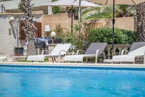 Un área junto a la piscina con sillones de descanso, una mesa y sombrillas.