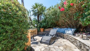 An outdoor patio with a stone floor, a lounge chair, a small table, and a potted plant.