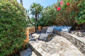 Un patio al aire libre con piso de piedra, una silla de descanso, una mesita y una planta en maceta.