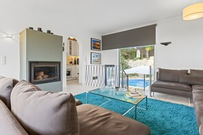 Una sala de estar moderna con chimenea, una mesa de centro de vidrio y vistas a una piscina.