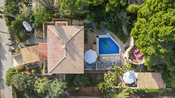 An aerial view of a property with a swimming pool, patio areas, and surrounding greenery.