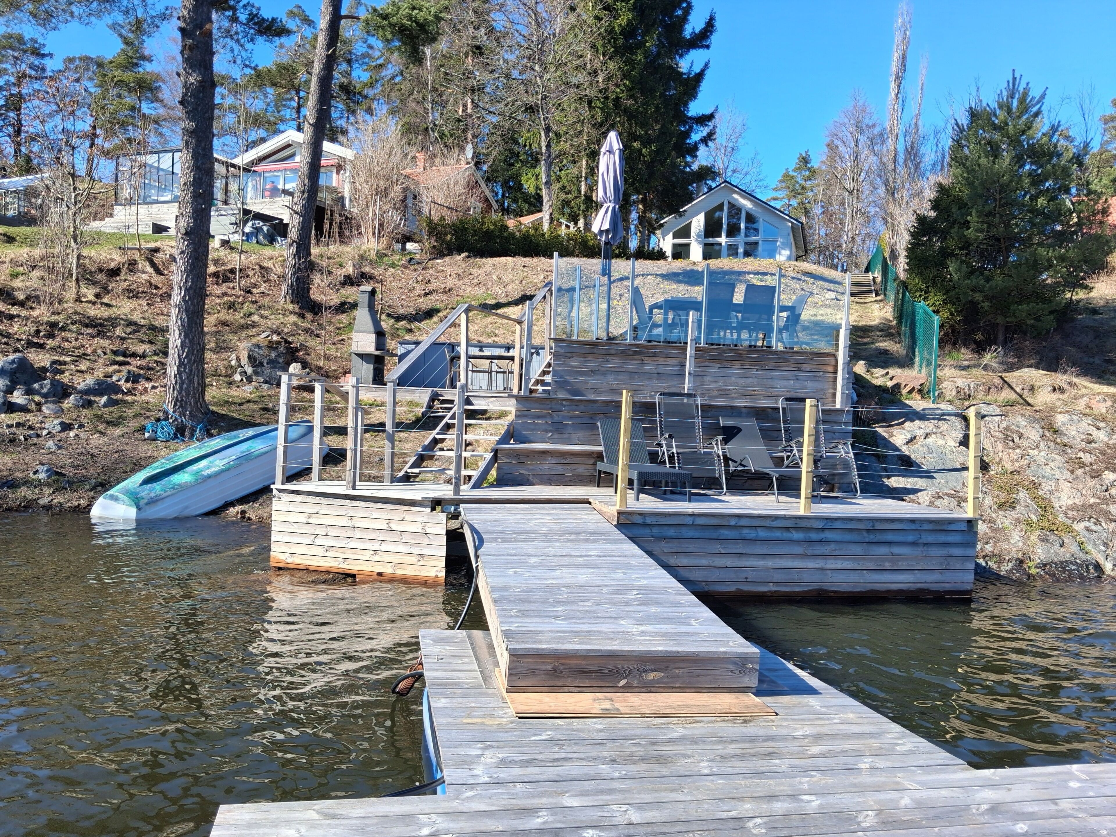 A wooden dock extending into a body of water with a small boat and a house in the background.
