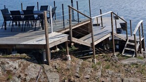 A wooden dock with a table and chairs, a covered area, and a view of a lake and distant buildings. - House on the waterfront, 15 minutes from downtown Stockholm (skogås)